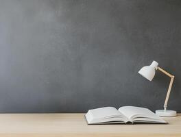 Higher education with students and policy concept. A minimal workspace featuring an open book and a desk lamp on a wooden surface against a gray wall. photo