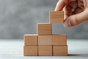 Motivation for entrepreneurship growth mindset concept. A hand stacking wooden blocks to create a pyramid shape on a textured surface. photo