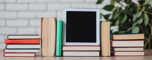 Higher education and innovation degree concept. A stack of books with a blank e-reader, set against a white brick background and greenery. photo