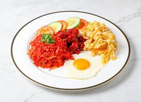 Spicy Fried Noodles with Fried Chicken, sunny side up egg Egg, loaded fries, fresh cucumber and tomato slices served in plate isolated on marble background side view of singapore breakfast food photo