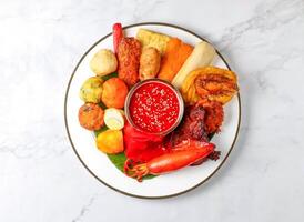 Malaysian Rojak set with Peanut Sauce, fried fritters, vegetables, tofu, sotong, and banana leaf served in plate isolated on marble background top view of singapore food photo