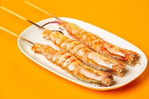 Grilled Tiger Prawns Skewers with salt served in plate isolated on orange background side view of hong kong food photo