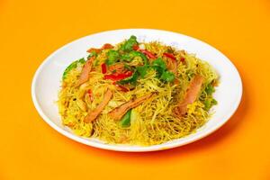Singapore Fried Rice Noodles including rice vermicelli stir fried with ham, vegetables, cilantro and red chilies served in plate isolated on orange background side view of hong kong food photo