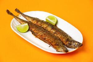 Grilled Capelin Fish or Saury Fish with Lime served in plate isolated on orange background side view of hong kong food photo