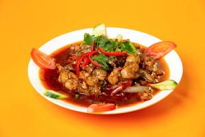 Spicy Frog Legs with Chili, tomato, coriander and cucumber served in plate isolated on orange background side view of hong kong food photo