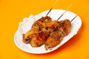 Crispy Grilled Chicken Wings on Skewers served in plate isolated on orange background side view of hong kong food photo