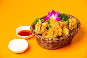 Crispy Fried Wontons with Dipping Sauces served in basket isolated on orange background side view of hong kong food photo