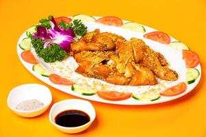 Crispy Fried Chicken garnished with fresh tomato and cucumber slices salt and soy sauce served in plate isolated on orange background side view of hong kong food photo
