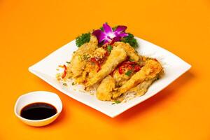 Salt and pepper fried fish with soy sauce, tomato and coriander served in plate isolated on orange background side view of hong kong food photo