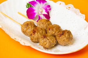 Roasted Beef Balls on Skewers served in plate isolated on orange background side view of hong kong food photo