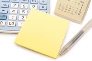 Blank Yellow Sticky note with calculator and calendar background. Financial data analyzing. Copy space for text on sticky note. isolated on white background. photo
