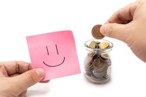 Saving money concept with Smiling faces drawn on pink sticky note. Happy to placing a coin into a jar.Commitment to achieving financial goals. isolated on white background. photo