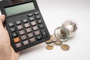 Thai Baht Coins spilled out of jar glass and Calculator with hand isolated on white background, saving for future, Investment business concept. photo