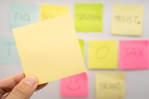 Hand holding Blank Sticky note with colorful sticky notes background. Copy space for text or infographic. photo