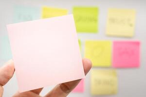 Hand holding Blank Pink Sticky note with colorful sticky notes background. Copy space for text or infographic. photo