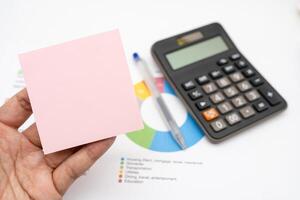Hand holding Blank Pink Sticky note with calculator background. Financial data analyzing. Working on desk with using calculator, finance accounting. Copy space. photo