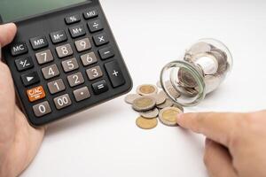 Thai Baht Coins spilled out of jar glass and Calculator with hand isolated on white background, saving for future, Investment business concept. Business and Financial Concept. photo