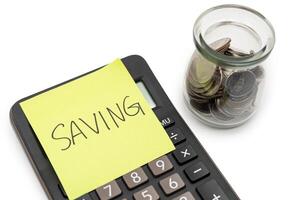 SAVING text with sticky note on calculator and Coins in glass money jar isolated on white background, financial concept. Saving money concept. photo