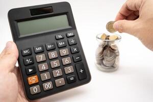 Saving money concept. Hand holding calculator and placing a coin into a jar. photo