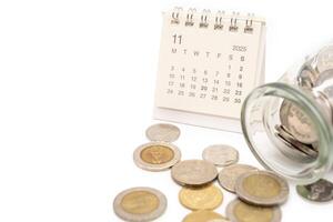 2025 NOVEMBER Calendar with Thai Baht Coins spilled out of jar glass isolated on white background, saving for future, Investment business concept. Copy Space. photo