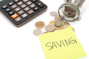 SAVING text with sticky note, calculator and Coins in glass money jar isolated on white background, financial concept. Saving money concept. photo