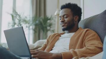 African american man relaxing on couch using laptop with copy space screen at home. Communication, technology, domestic life and lifestyle, unaltered photo