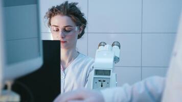 A scientist analyzes a sample under a microscope in a medical laboratory, researching data for new discoveries. The concept of an ambitious biotechnology specialist working with innovative equipment video
