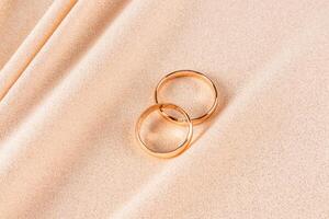 Two classic gold wedding rings lie on a chic gold-colored fabric with glitter. Soft folds of fabric flow from bottom to top. Wedding design. layout. photo