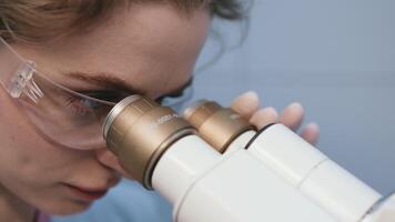 Frau Wissenschaftler Analysen ein Stichprobe unter ein Mikroskop im ein medizinisch Labor, recherchieren Daten zum Neu Entdeckungen. das Konzept von ein ehrgeizig Biotechnologie video