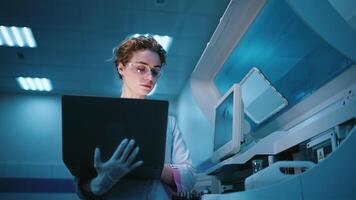 Female robotics engineer with a laptop analyzing the concept of a robotic machine in a state-of-the-art lab. The concept of programming and data tracking to optimize robot performance video