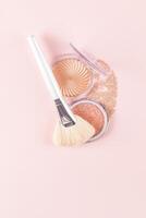 A large white fan brush for applying makeup lies on two open packs of different highlighter and a smeared texture swatch. The top vertical view. photo