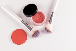 Two chic makeup brushes and two blush in an open jar, a pink tone block on a white embossed background. top view. A copy space. The concept of beauty. photo