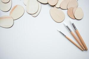 Wooden Easter egg shapes and paintbrushes on white background with copy space for creative art projects photo