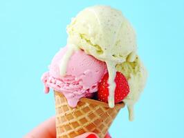 Delightful summer treat. Hand holding dripping ice cream cone with strawberry photo