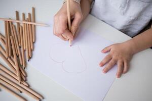 Child drawing heart with pencils on paper photo