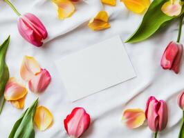 Blank white card surrounded by colorful tulip petals on fabric background photo