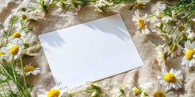 Blank white card on linen fabric surrounded by chamomile flowers for floral invitation design photo