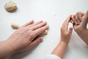 Caucasian adult and child hands working with dough on white surface photo