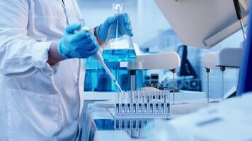 Hands of scientist in blue gloves analyzes a blue liquid in a flask, adding drops from a pipette. Chemical substances and modern research methods. Nobody, advertising, banner video