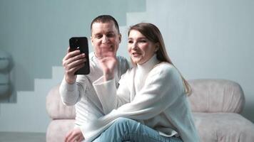 A couple is talking on a social media call on their phone in living room at home on the couch. Concept modern communication and closeness, creating a cozy atmosphere in family life using technology video