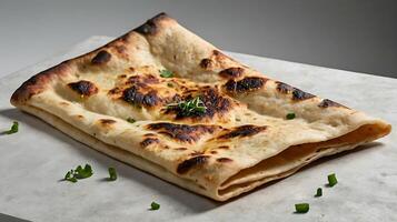 Closeup view of a folded flatbread with charred spots on a light surface photo