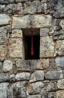 A red rope is hanging from the window of an ancient stone wall. photo