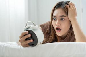Shocked Asia young woman looking at clock alarm, lady is late appointment or work or class study, overslept, difficulty get up in mornings, time worried, not on time, sleepy, over due photo