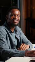 Vertical POV of african american guy attending an online conference from his home office in loft. Male speaker discussing work remotely with coworkers using wireless tech for call. Camera B. video