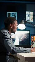 Vertical Black young adult working remotely and organizing information, reviewing notes and making data driven decisions to complete his freelancing tasks. Managing his schedule efficiently. Camera A. video