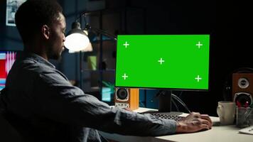 African american adult working from home using chroma key mockup, reviewing statistical data to compare supply and demand numbers. Sitting at desk and writing on his computer. Camera A. video