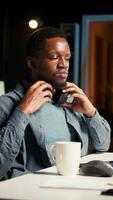 Vertical African american specialist closing the monthly balance with a show on headset, working remotely while he listens to his favorite podcast. Managing expenses and insurances from home. Camera A. video