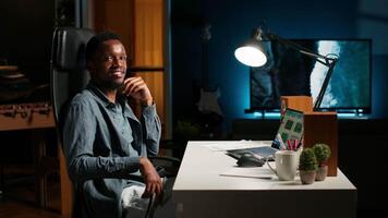 Black young adult working remotely and organizing information, reviewing notes and making data driven decisions to complete his freelancing tasks. Managing his schedule efficiently. Camera B. video