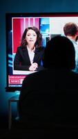 Vertical Curious spectator reading news coverage titles on smart tv set, sitting on couch and listening to journalist lay out recent global events. Guy watching daily news headlines, tv content. Camera B. video