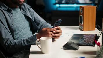 African american man listening to music and browsing webpages on his mobile phone, scrolling through social media apps and taking break from solving tasks at the desk. Answering texts. Camera B. video